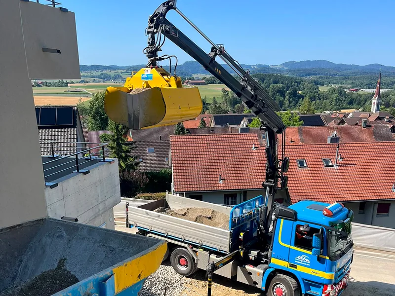 Kran mit Greifer verteilt Kies auf einer Hangbaustelle