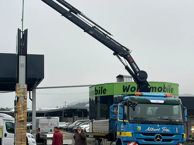 Kranwagen montiert eine Werbetafel an einem Mast