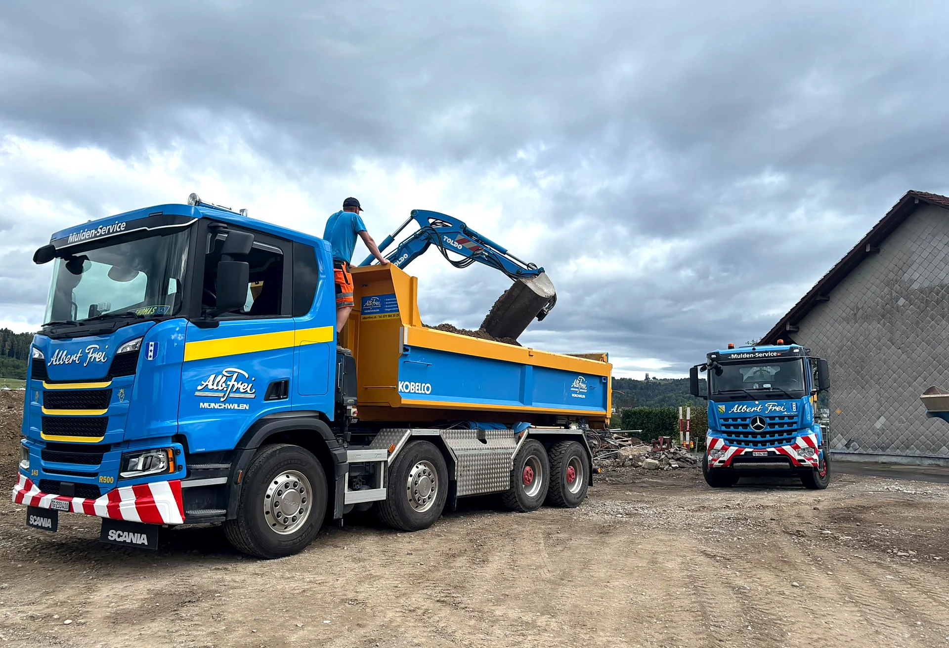 Scania-Muldenlastwagen von Alb. Frei wird mit Aushub beladen, dahinter ein Mercedes-Muldenwagen